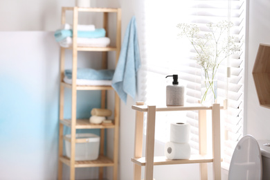 Soap dispenser and toilet paper on wooden stand in bathroom