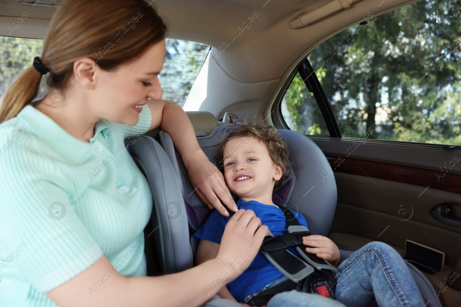 Photo of Mother fastening her son in child safety seat inside car