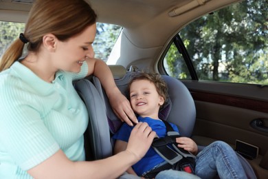 Mother fastening her son in child safety seat inside car