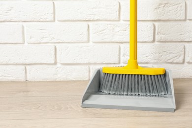 Photo of Plastic broom with dustpan near white brick wall indoors. Space for text