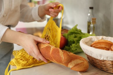 Woman taking baguette out from string bag at countertop, closeup