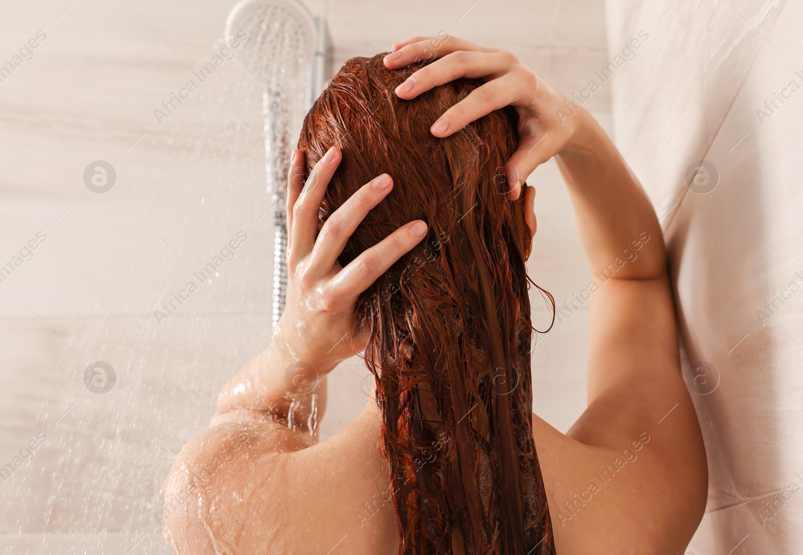 Photo of Young woman washing her hair with shampoo in shower, back view