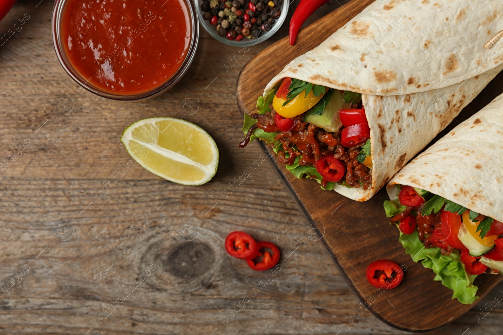 Photo of Board with delicious meat tortilla wraps on wooden table, flat lay