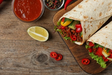 Board with delicious meat tortilla wraps on wooden table, flat lay