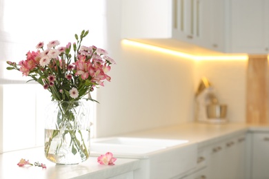 Vase with beautiful flowers on kitchen counter, space for text. Stylish element of interior design