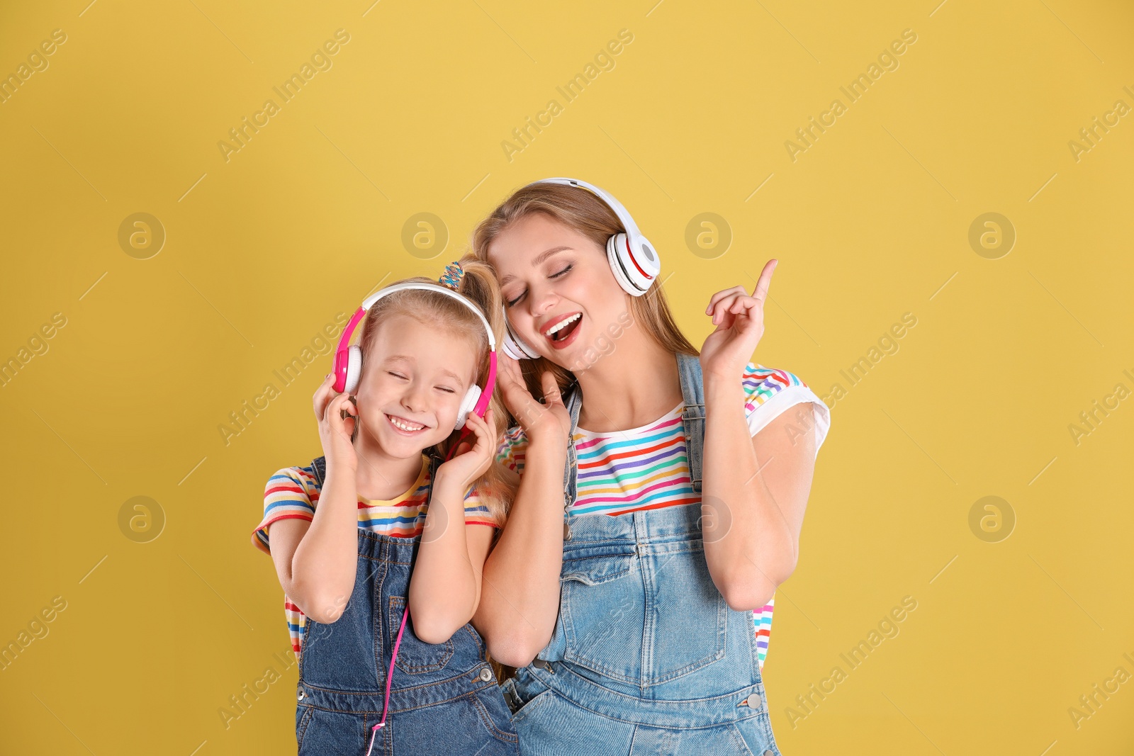 Photo of Happy mother and little daughter with headphones on yellow background