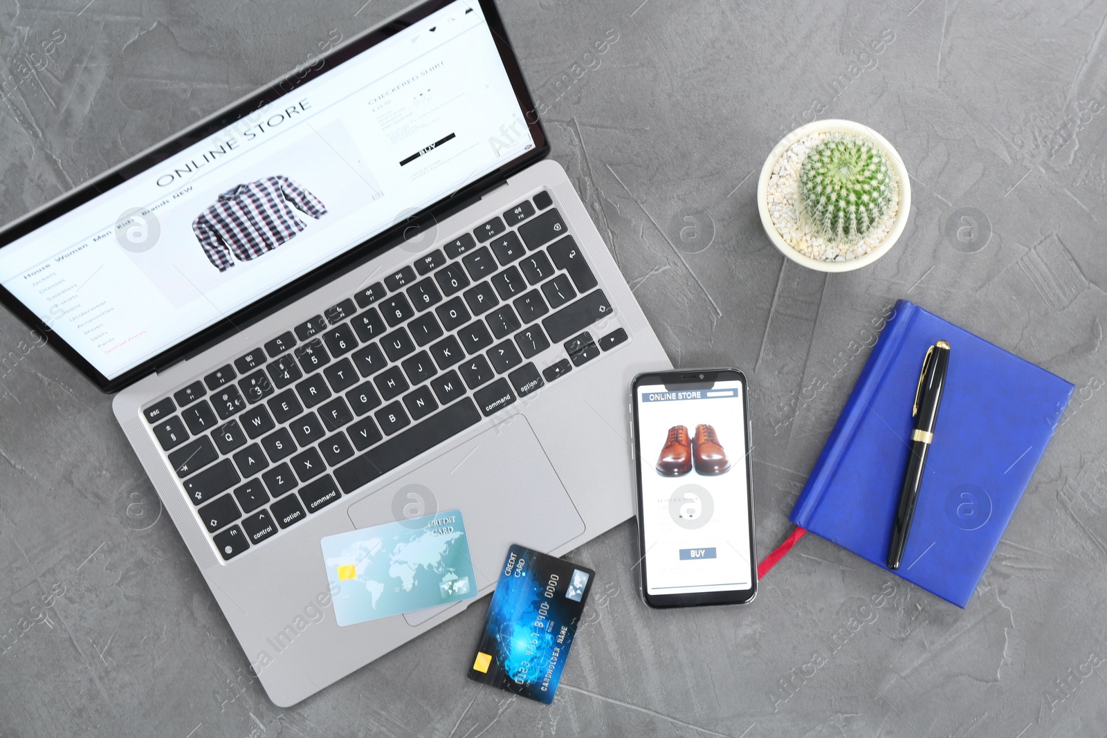 Photo of Online store website on laptop screen. Computer, smartphone, stationery, credit cards and cactus on grey table, flat lay