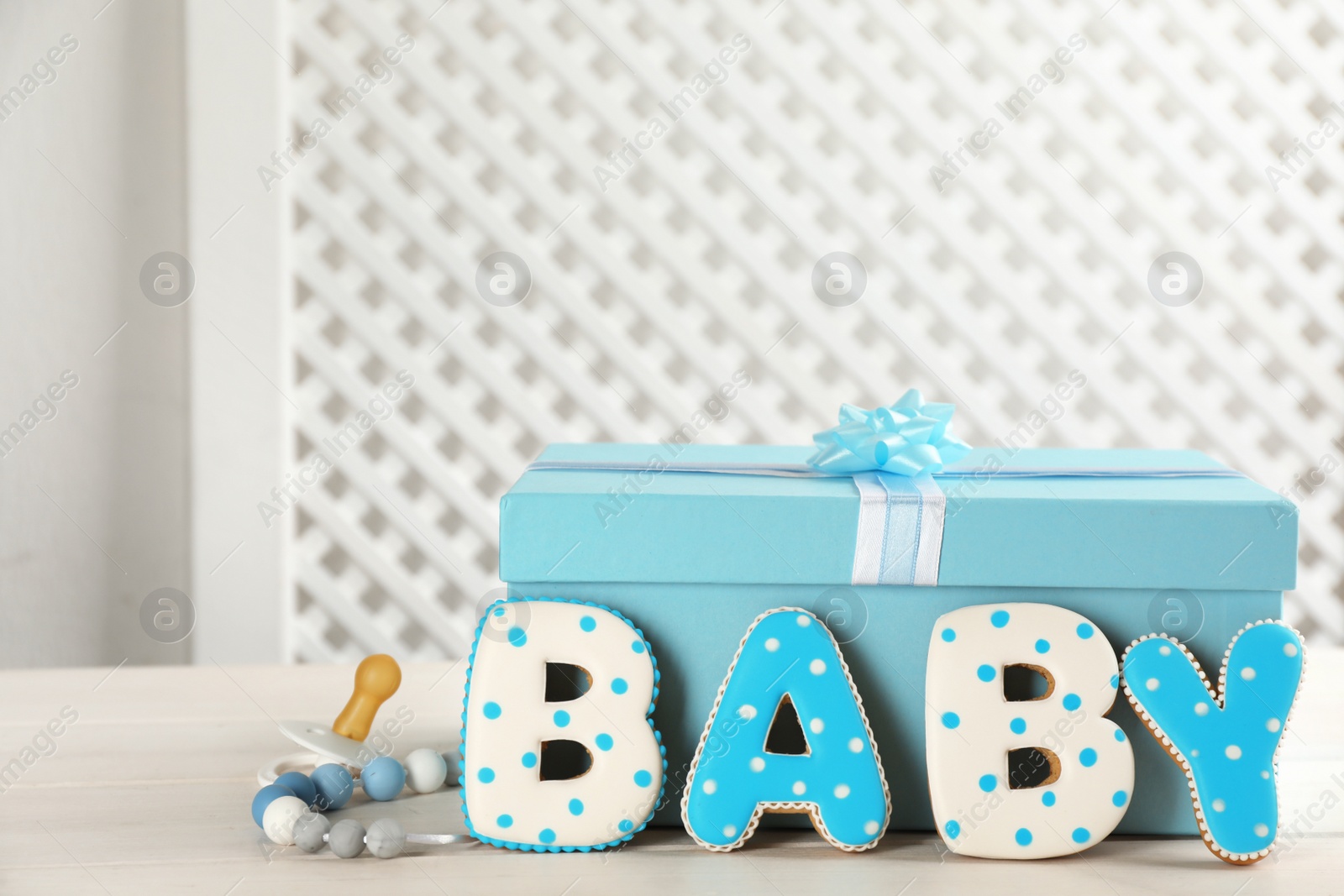 Photo of Word Baby made of tasty cookies, gift box and pacifier on white wooden table. Space for text