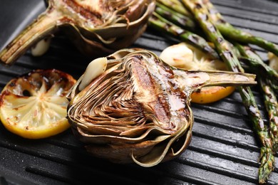 Photo of Tasty grilled artichokes, asparagus and slices of lemon in pan, closeup