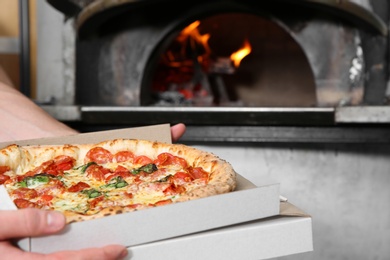 Photo of Chef holding delivery box with traditional oven baked Italian pizza in kitchen restaurant, closeup
