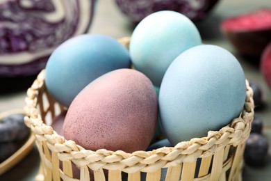 Photo of Colorful Easter eggs painted with natural dyes in wicker bowl, closeup