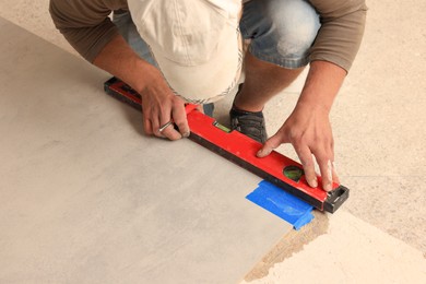 Photo of Worker measuring tile with building level indoors