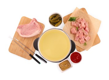 Oil in fondue pot, forks, pickles, sauces and pieces of raw meat isolated on white, top view
