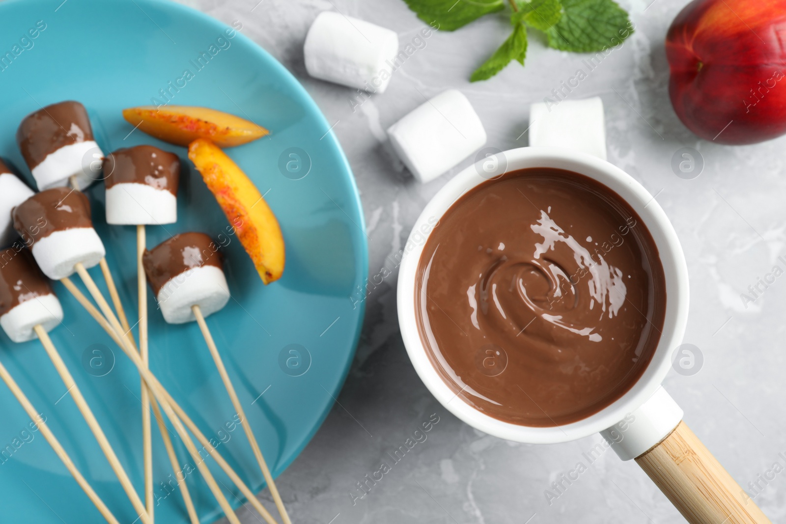 Photo of Fondue pot with milk chocolate and marshmallows on marble table, top view