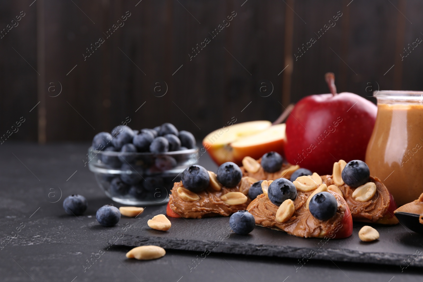 Photo of Fresh apples with peanut butter and blueberries on dark table