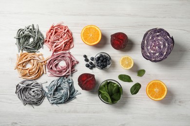 Rolled pasta painted with natural food colorings and ingredients on white wooden table, flat lay