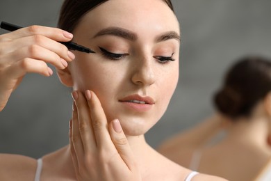 Makeup product. Woman applying black eyeliner on blurred background, closeup