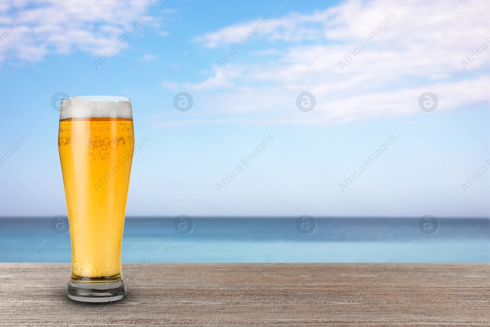 Image of Cold beer on wooden desk against blurred sea. Space for text