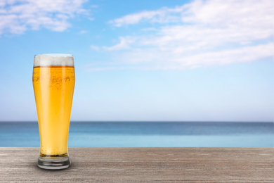 Image of Cold beer on wooden desk against blurred sea. Space for text