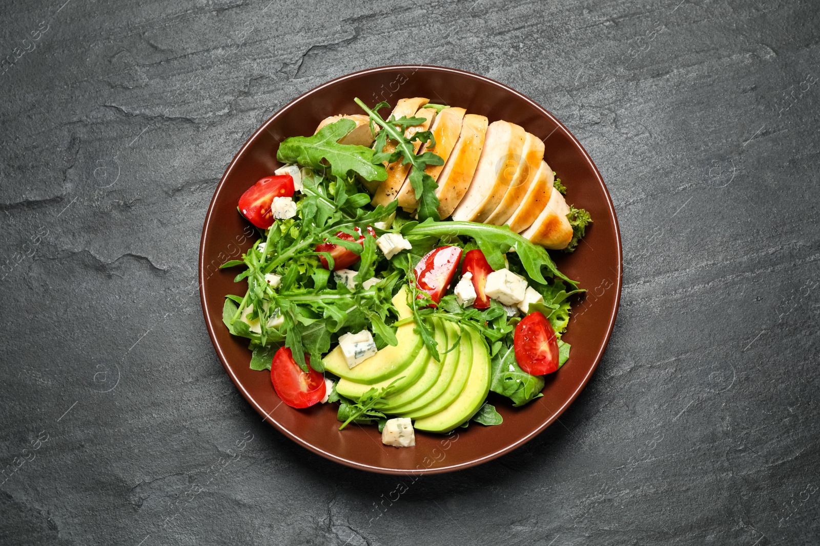 Photo of Delicious salad with chicken, arugula and avocado on black table, top view