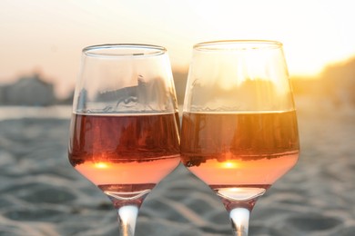 Glasses of tasty rose wine on sandy beach, closeup