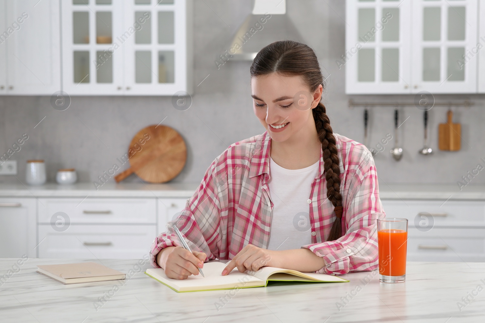 Photo of Beautiful young woman writing in notebook at white marble table indoors