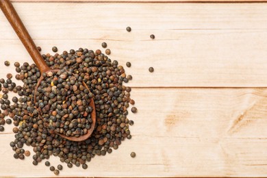 Photo of Spoon and many raw lentils on light wooden table, top view. Space for text