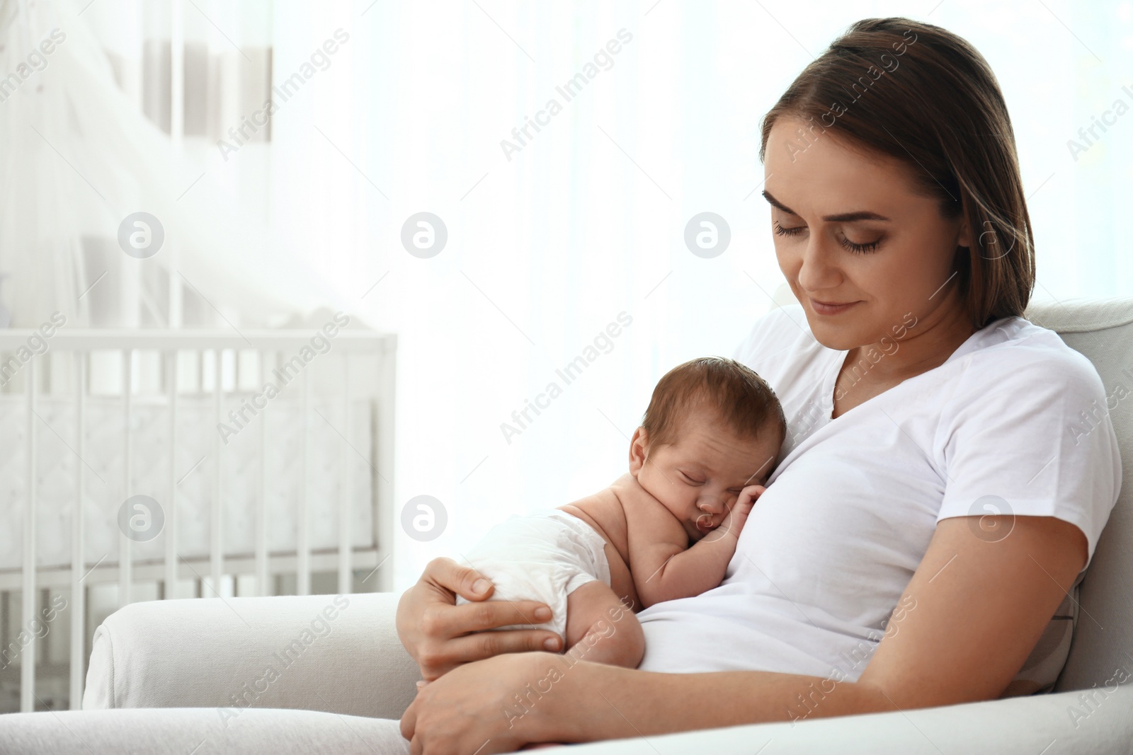 Photo of Young mother with her little baby sitting in armchair at home. Space for text