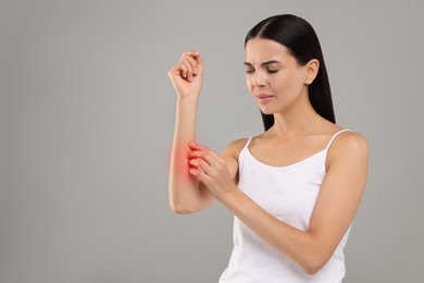 Photo of Suffering from allergy. Young woman scratching her arm on light grey background. Space for text