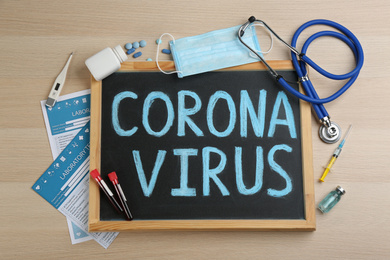 Chalkboard with words CORONA VIRUS, stethoscope and medicines on wooden background, flat lay