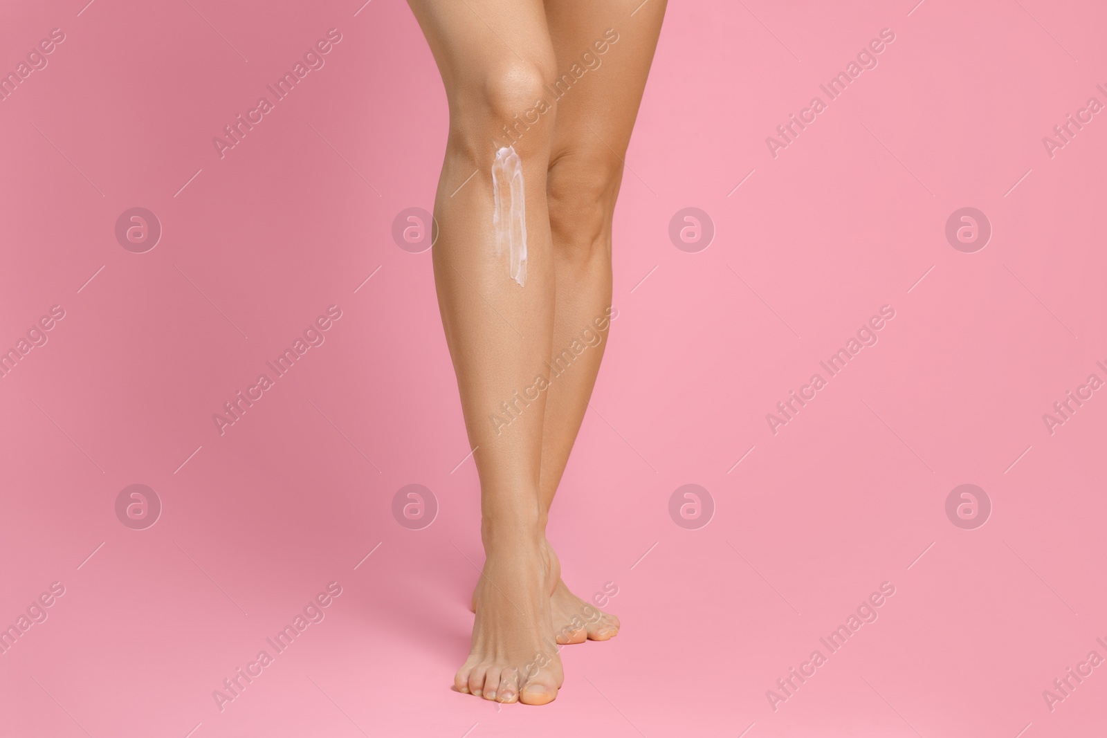 Photo of Woman with body cream on her leg against pink background, closeup
