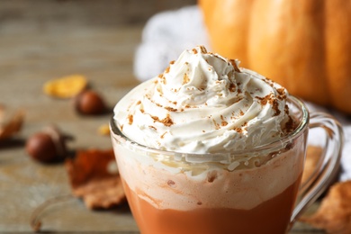Pumpkin spice latte with whipped cream in glass cup on table, closeup