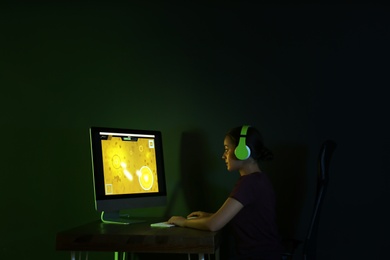 Photo of Young woman with headphones playing video game in dark room