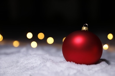 Photo of Christmas ball and fairy lights on white snow outdoors. Space for text