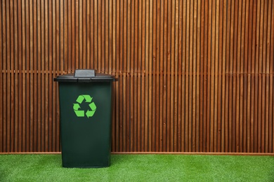 Photo of Trash bin with recycling symbol near wooden wall indoors. Space for text