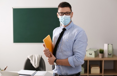 Photo of Teacher with protective mask, glasses and copybook in classroom. Reopening after Covid-19 quarantine
