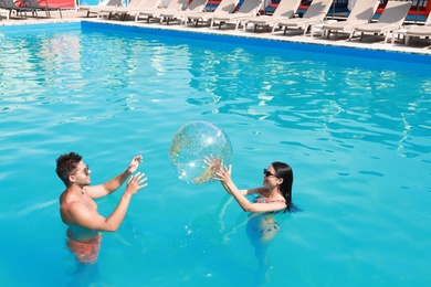 Photo of Woman in bikini and her boyfriend playing with inflatable ball at resort. Happy young couple