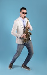 Young man playing saxophone on light blue background