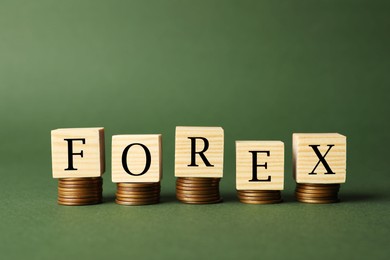 Photo of Word Forex made of wooden cubes with letters on stacked coins against green background