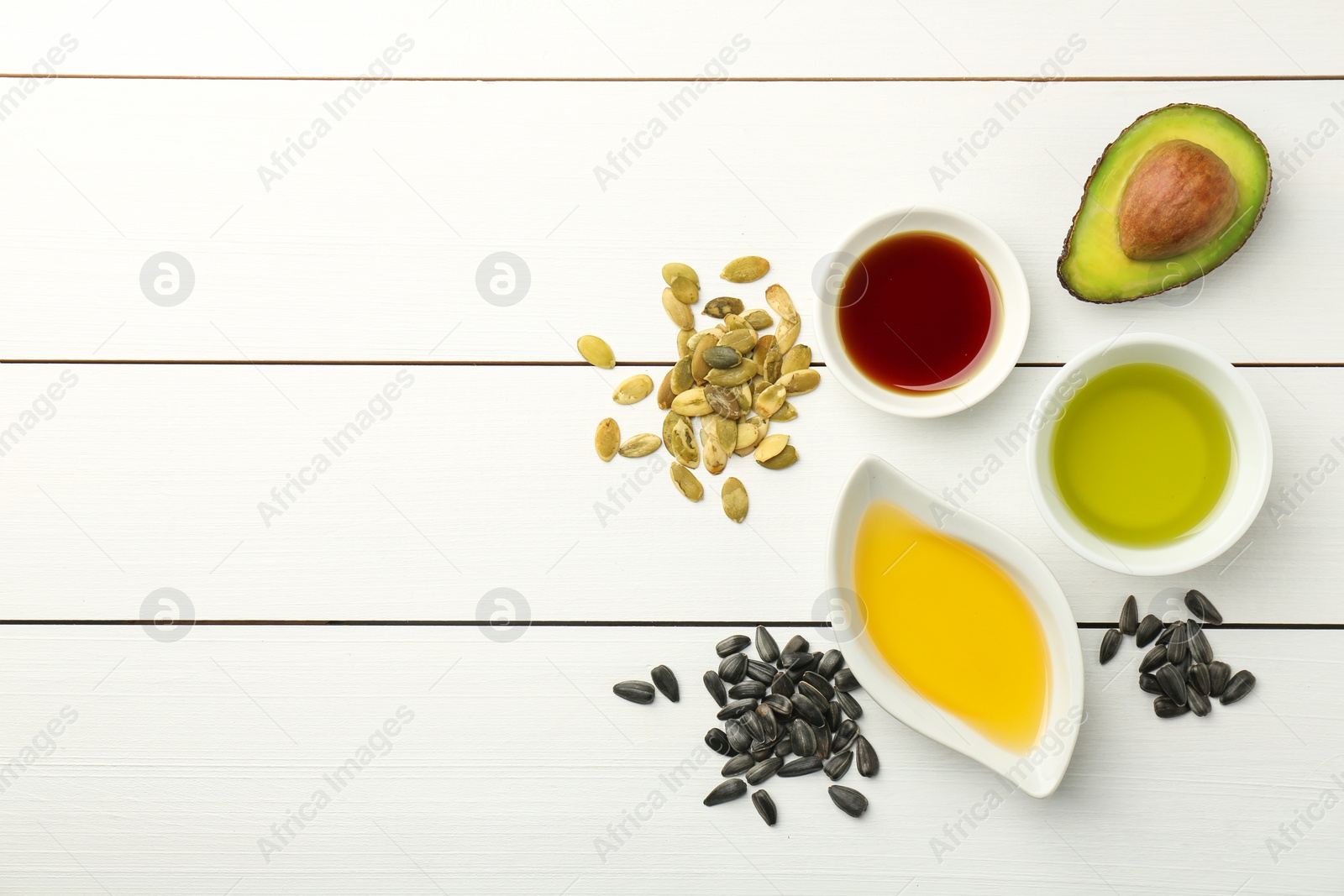 Photo of Vegetable fats. Different cooking oils in bowls and ingredients on white wooden table, flat lay. Space for text