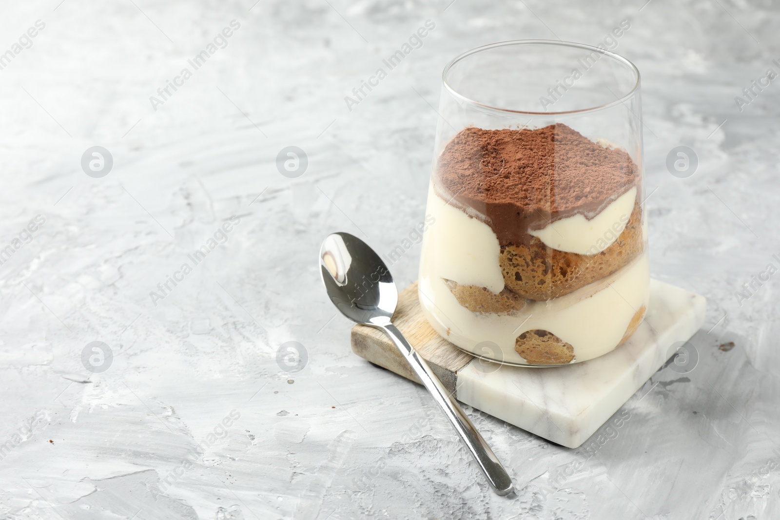 Photo of Delicious tiramisu in glass and spoon on grey textured table, space for text