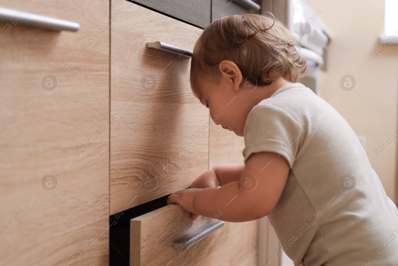 Photo of Little child exploring drawer indoors. Dangerous situation