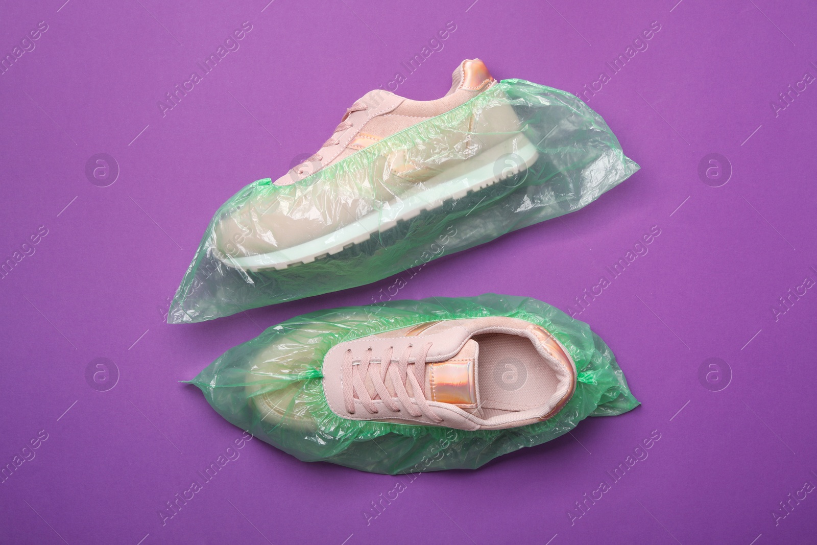 Photo of Sneakers in shoe covers on purple background, top view