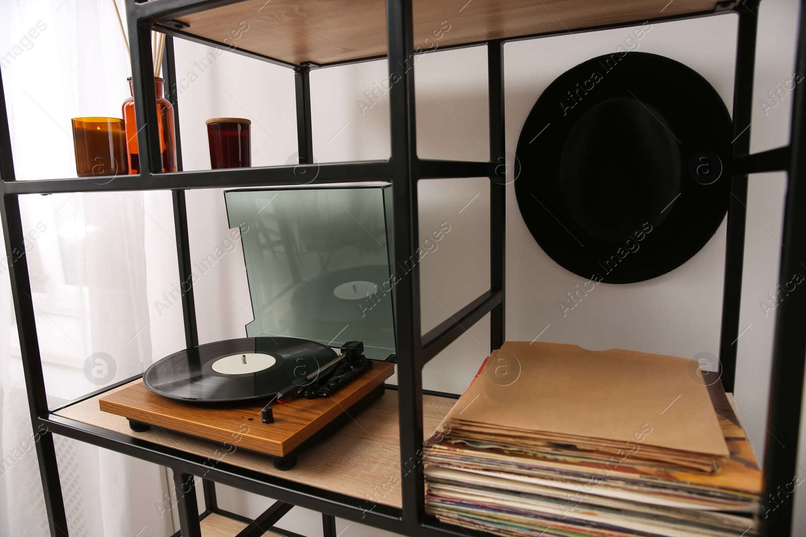 Photo of Stylish turntable with vinyl record on shelving unit indoors