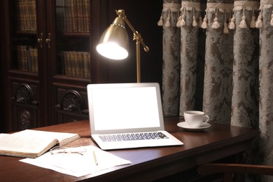 Photo of Laptop, book and papers on wooden table in library reading room