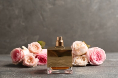 Photo of Bottle of perfume with beautiful roses on table, space for text