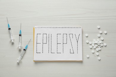 Photo of Notebook with word Epilepsy, pills and syringes on white wooden table, flat lay