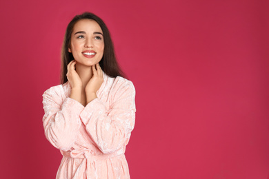 Beautiful young woman in bathrobe on crimson background. Space for text