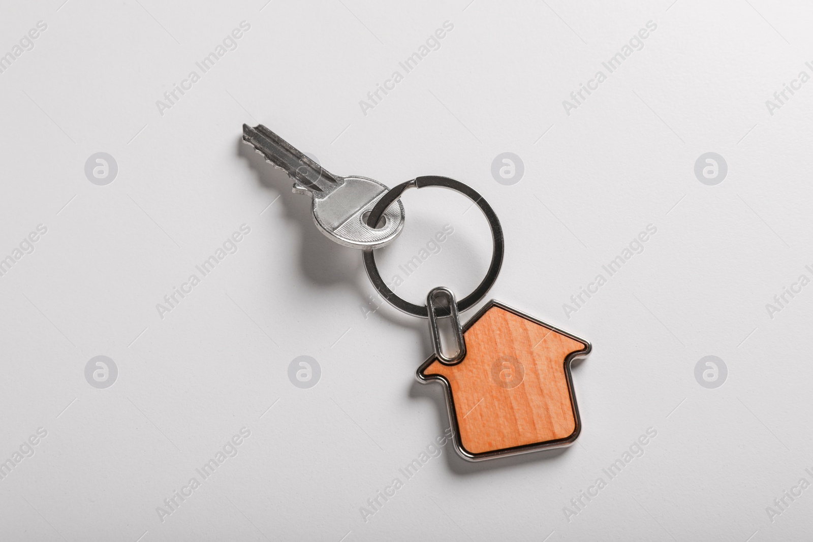 Photo of Key with trinket in shape of house on white background, top view. Real estate agent services