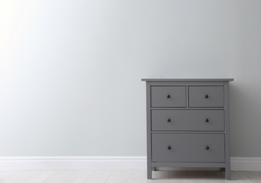 Photo of Modern grey chest of drawers near light wall in room, space for text. Interior design